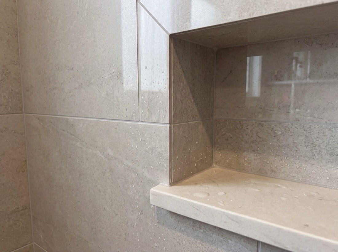 A tiled shower niche with mitered edges and a solid stone shelf
